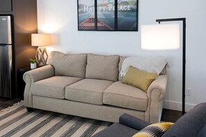 A beige sofa with a patterned pillow, a lamp, and a framed picture on the wall. - Deluxe Lofted Cabin Ideal for Families in Livingston, Texas (Livingston)