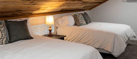 A bedroom with two beds, a nightstand with a lamp, and a wooden ceiling.