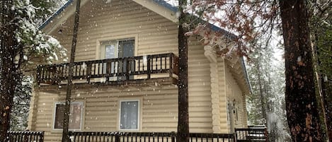 A log cabin with a balcony, surrounded by trees and covered in snow.