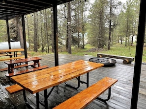 Eine überdachte Holzterrasse mit Picknicktischen und einem Feuerkorb.