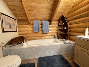 Ein Badezimmer einer Holzhütte mit einer Badewanne, Handtüchern, einem Ablagefach für Toilettenartikel und einem gerahmten Bild an der Wand.