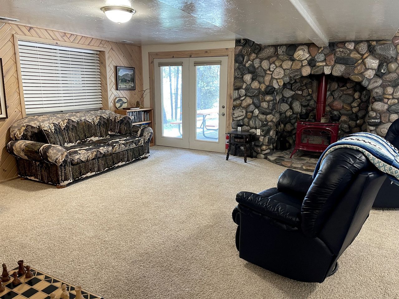 A living room with a stone fireplace, a sofa, a recliner, and a chessboard.