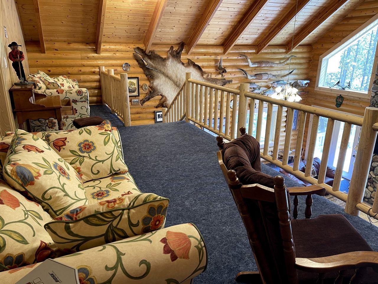 L’intérieur d’une cabane en rondins, avec un canapé, un fauteuil, une peau d’animal décorative accrochée au mur et une fenêtre donnant sur la forêt.