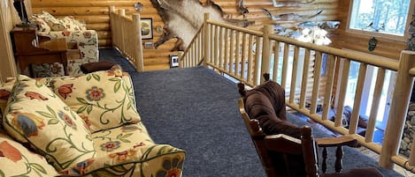 L’intérieur d’une cabane en rondins, avec un canapé, un fauteuil, une peau d’animal décorative accrochée au mur et une fenêtre donnant sur la forêt.