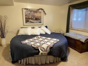 Ein Schlafzimmer mit einem großen Bett, einem Gemälde eines Leuchtturms, einem Nachttisch und einem Fenster mit Vorhängen.
