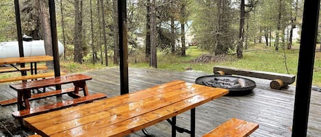 A covered wooden deck with picnic tables and a fire pit.