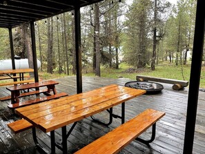 Eine überdachte Holzterrasse mit Picknicktischen und einem Feuerkorb.