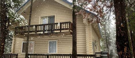 A log cabin with a balcony, surrounded by trees and covered in snow.