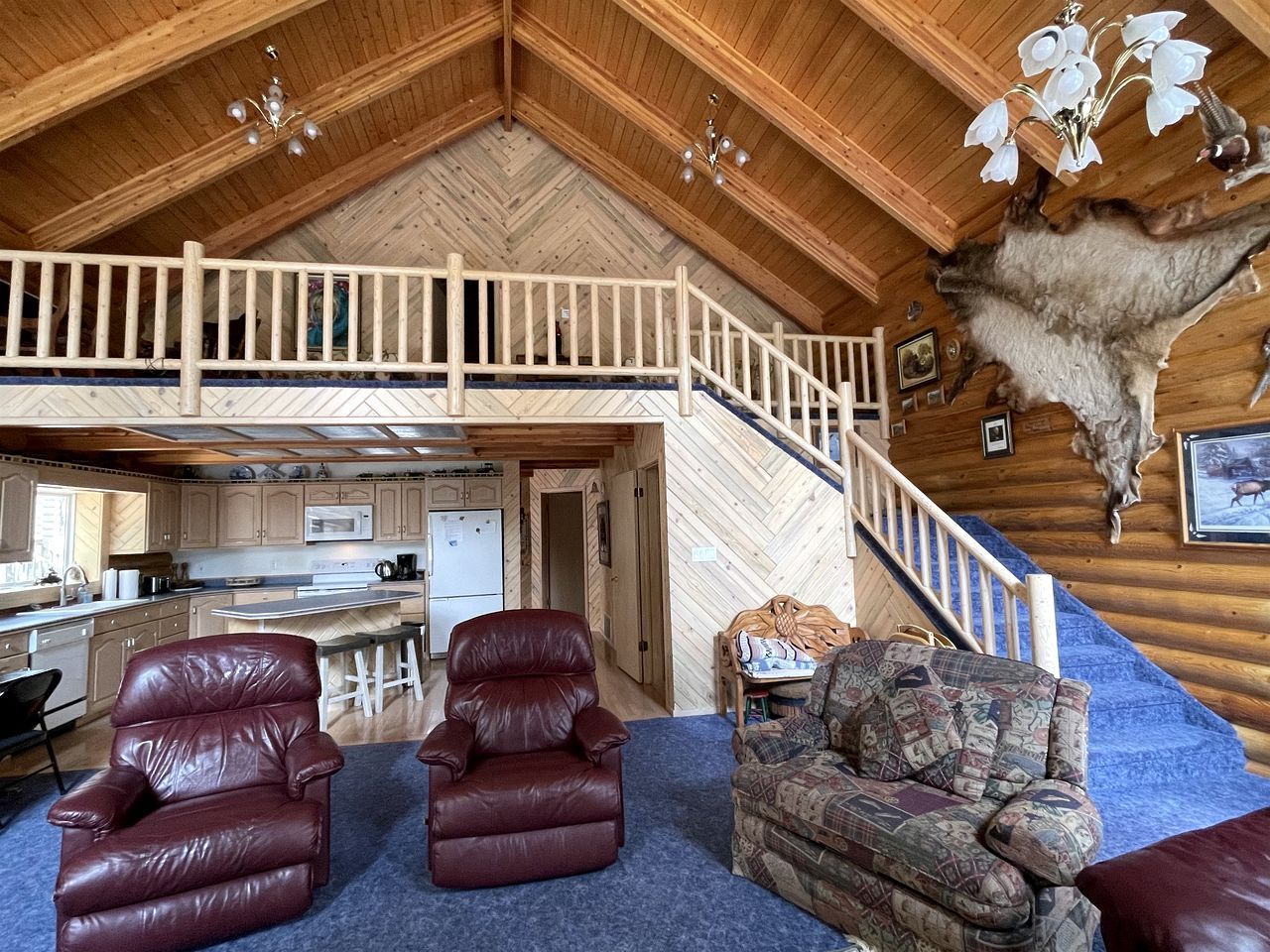 L’intérieur d’une cabane en rondins, avec un escalier en bois, des fauteuils en cuir, un canapé à motifs, un coin cuisine et une peau d’animal fixée au mur.