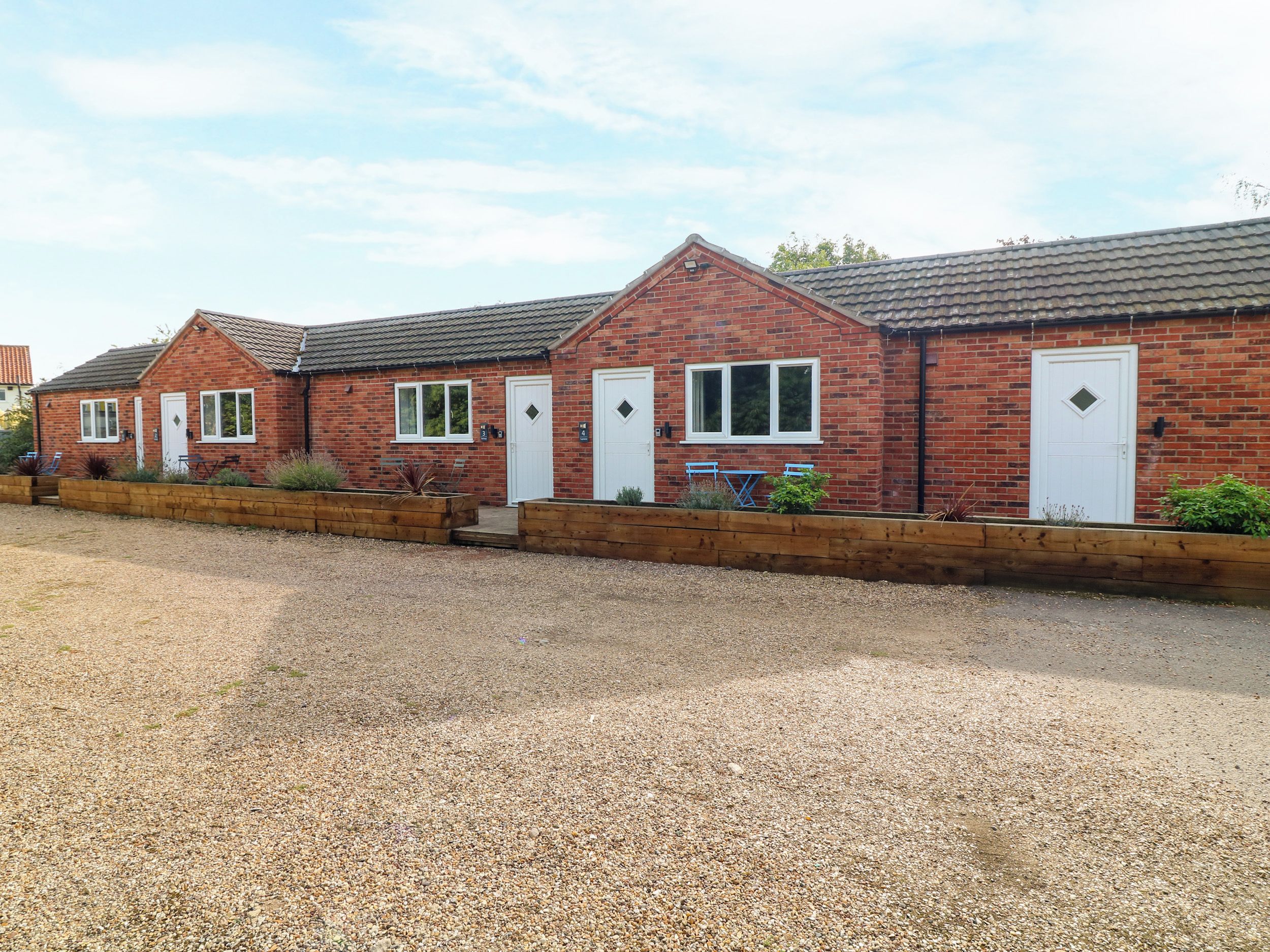 A brick building with two white doors, a gravel driveway, and wooden planters.