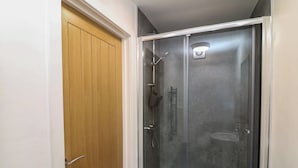 Une douche à l’italienne avec une porte en verre, une porte en bois adjacente et un petit porte-serviettes fixé au mur.