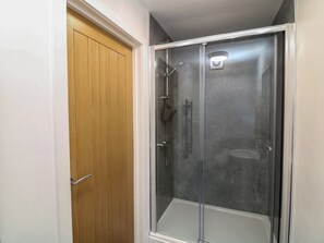 Eine bodenebene Dusche mit Glastür, eine angrenzende Holztür und ein kleiner Handtuchhalter an der Wand.