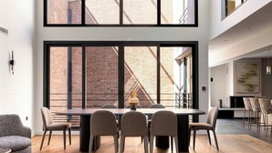Zona pranzo moderna con un tavolo grande e sedie, una parete in mattoni e vista su un edificio.