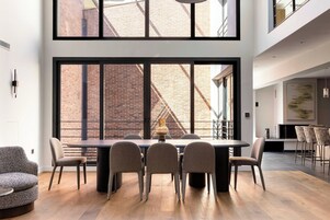 A modern dining area with a large table and chairs, a brick wall, and a view of a building.
