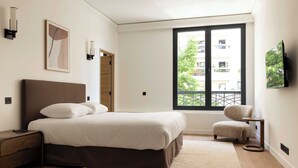 Una camera da letto con un letto, un comodino, una sedia, una finestra e opere d'arte.