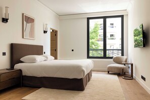 Ein Schlafzimmer mit Bett, Nachttisch, Stuhl, Fenster und einem Kunstwerk.