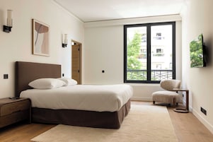 A bedroom with a bed, bedside table, chair, window, and artwork.