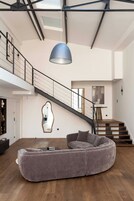 A spacious living area with a large, curved gray sofa, a staircase with a black railing, and a skylight above.