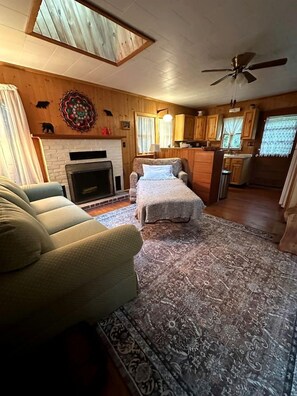 A cozy living room with a fireplace, a sofa, a bed, and a kitchen area with wooden cabinets and a ceiling fan.