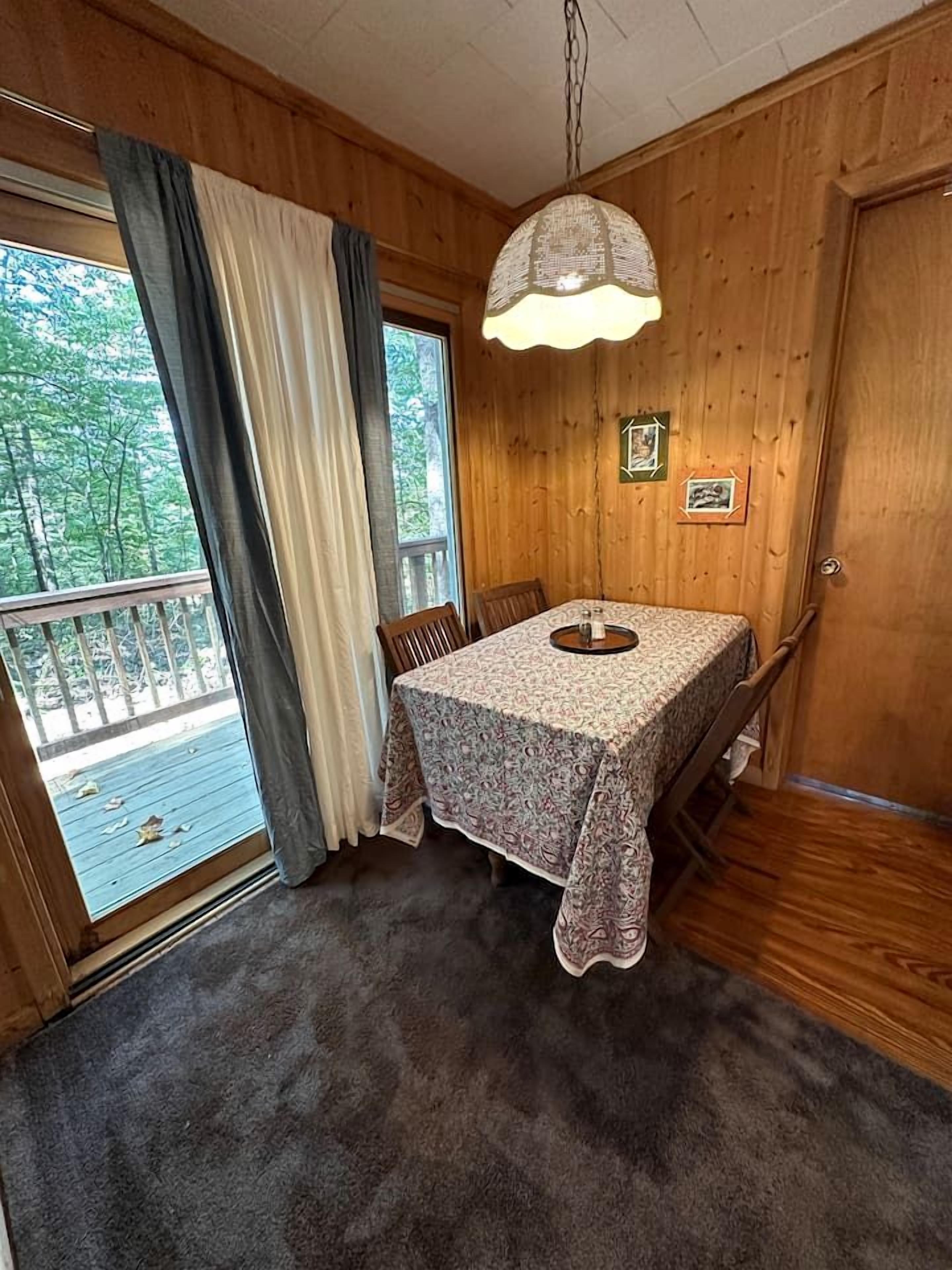 A wooden room with a table and chairs, a hanging light fixture, and a view through a window.