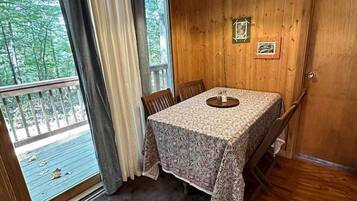 A wooden room with a table and chairs, a hanging light fixture, and a view through a window.