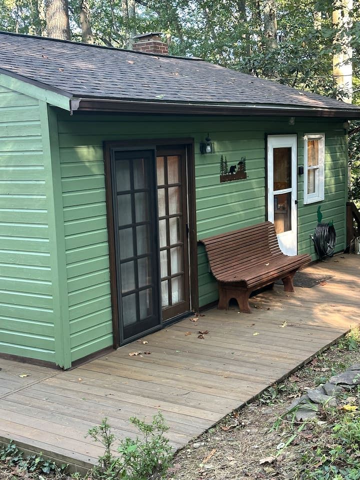 A green house with a wooden deck, a bench, and a door.
