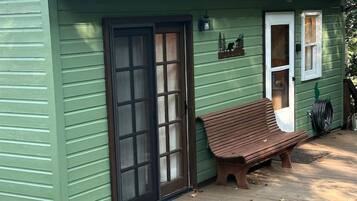 A green house with a wooden deck, a bench, and a door.
