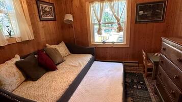 A wooden-paneled room with a bed, dresser, and windows.