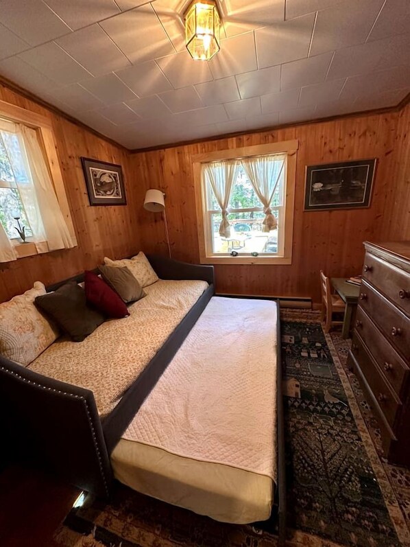 A wooden-paneled room with a bed, dresser, and windows.