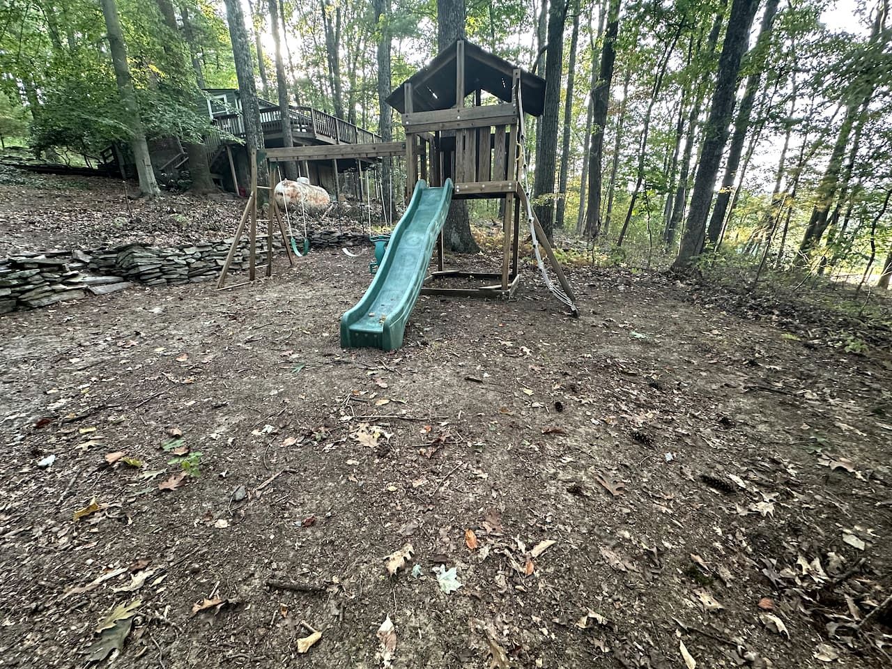 A playground with a slide and climbing structures in a wooded area.