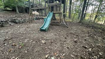 A playground with a slide and climbing structures in a wooded area.