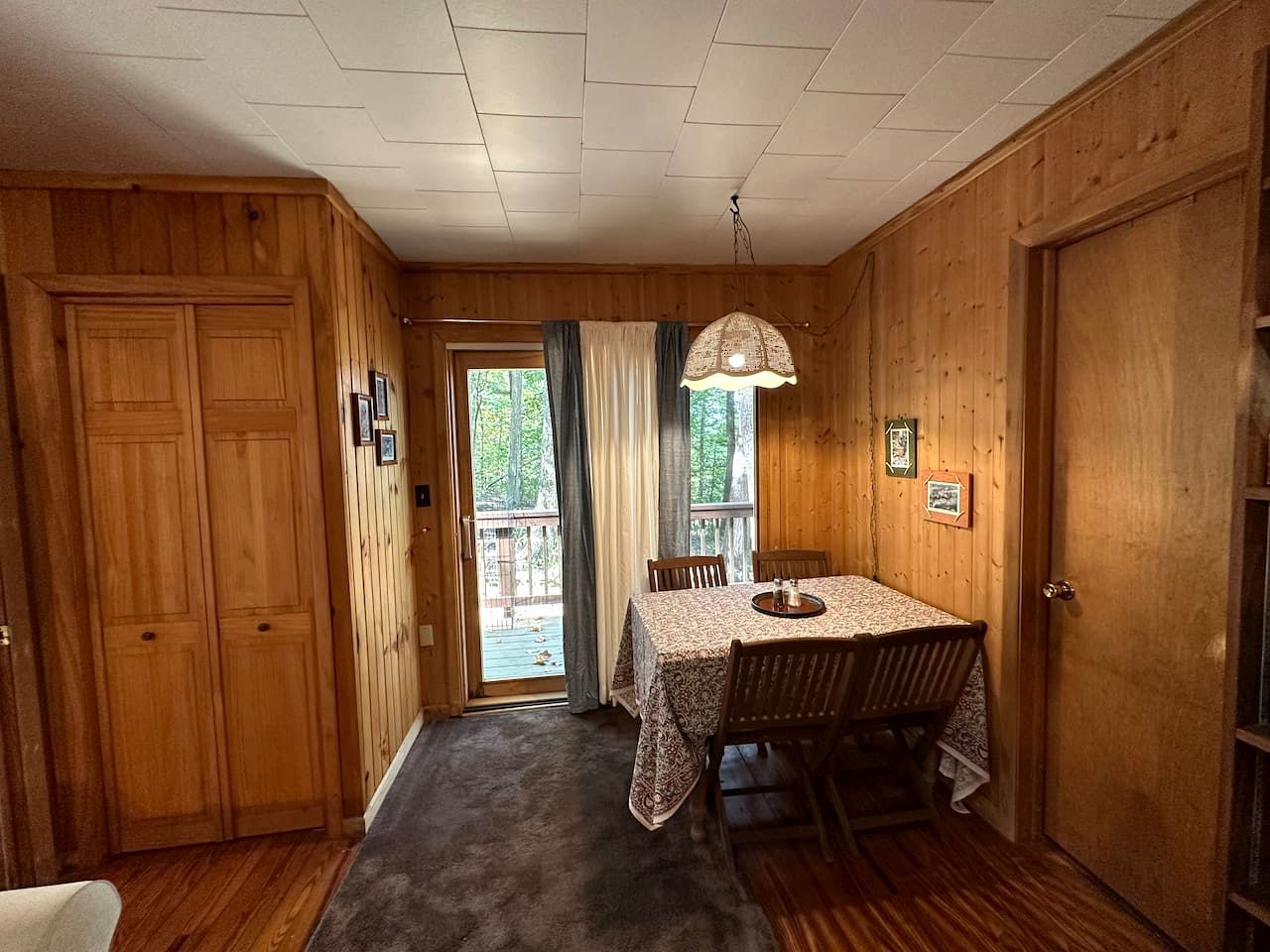 A wooden interior with a dining table, chairs, a chandelier, and a door leading to an outdoor area.