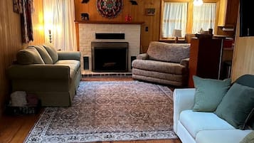 A living room with a fireplace, two sofas, a rug, and wooden floors.
