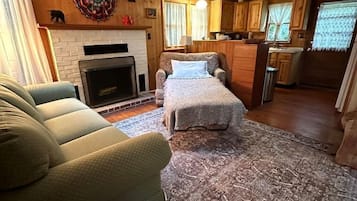 A cozy living room with a fireplace, a sofa, a bed, and a kitchen area with wooden cabinets and a ceiling fan.