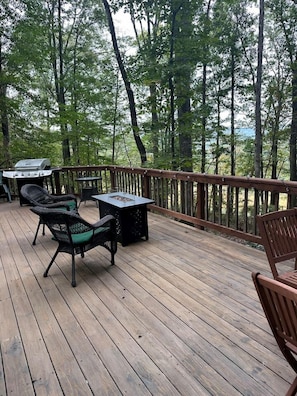 Eine Holzterrasse mit Gartenmöbeln, einem Grill und Blick auf einen Wald.