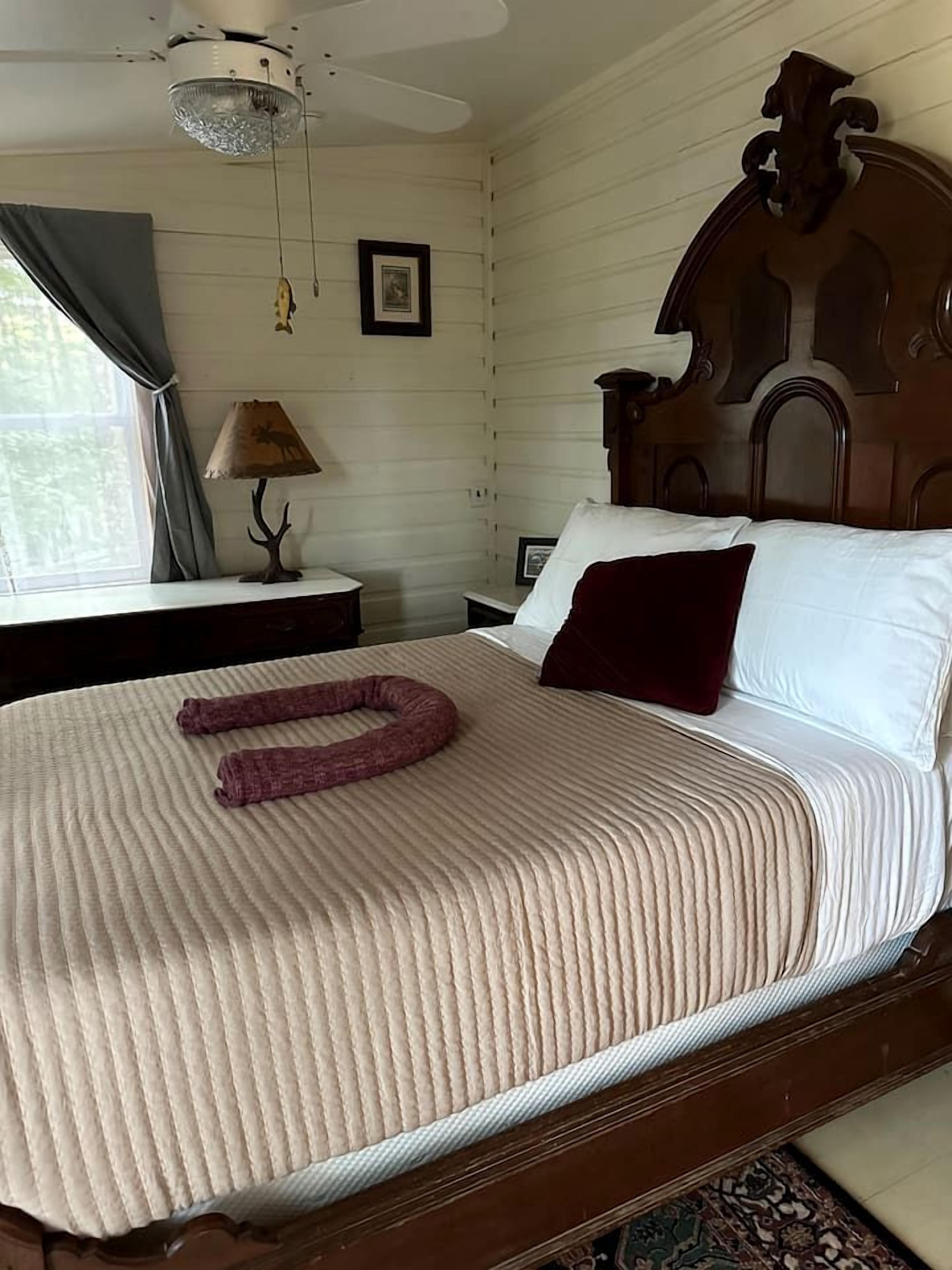 A neatly made bed with a patterned bedspread, a wooden headboard, a bedside lamp, and a framed picture on the wall.