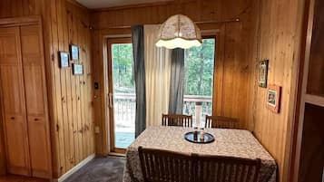 Ein Holzinterieur mit Esstisch, Stühlen, einer Pendelleuchte und einer zur Außenwelt führenden Tür.