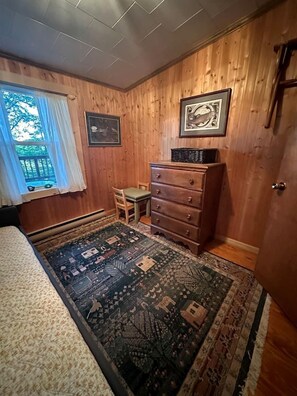 A room with wooden paneled walls, a bed, a dresser, a chair, and a rug.