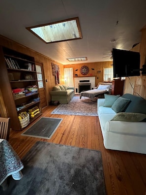 A cozy living room with a fireplace, a sofa, a bookshelf, and a television. - Hidden Countryside Gem with Fire Pit & Tranquil Setting in Aspers, Pennsylvania (Aspers)