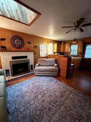 A living room with a fireplace, patterned rug, and a ceiling fan. - Hidden Countryside Gem with Fire Pit & Tranquil Setting in Aspers, Pennsylvania (Aspers)
