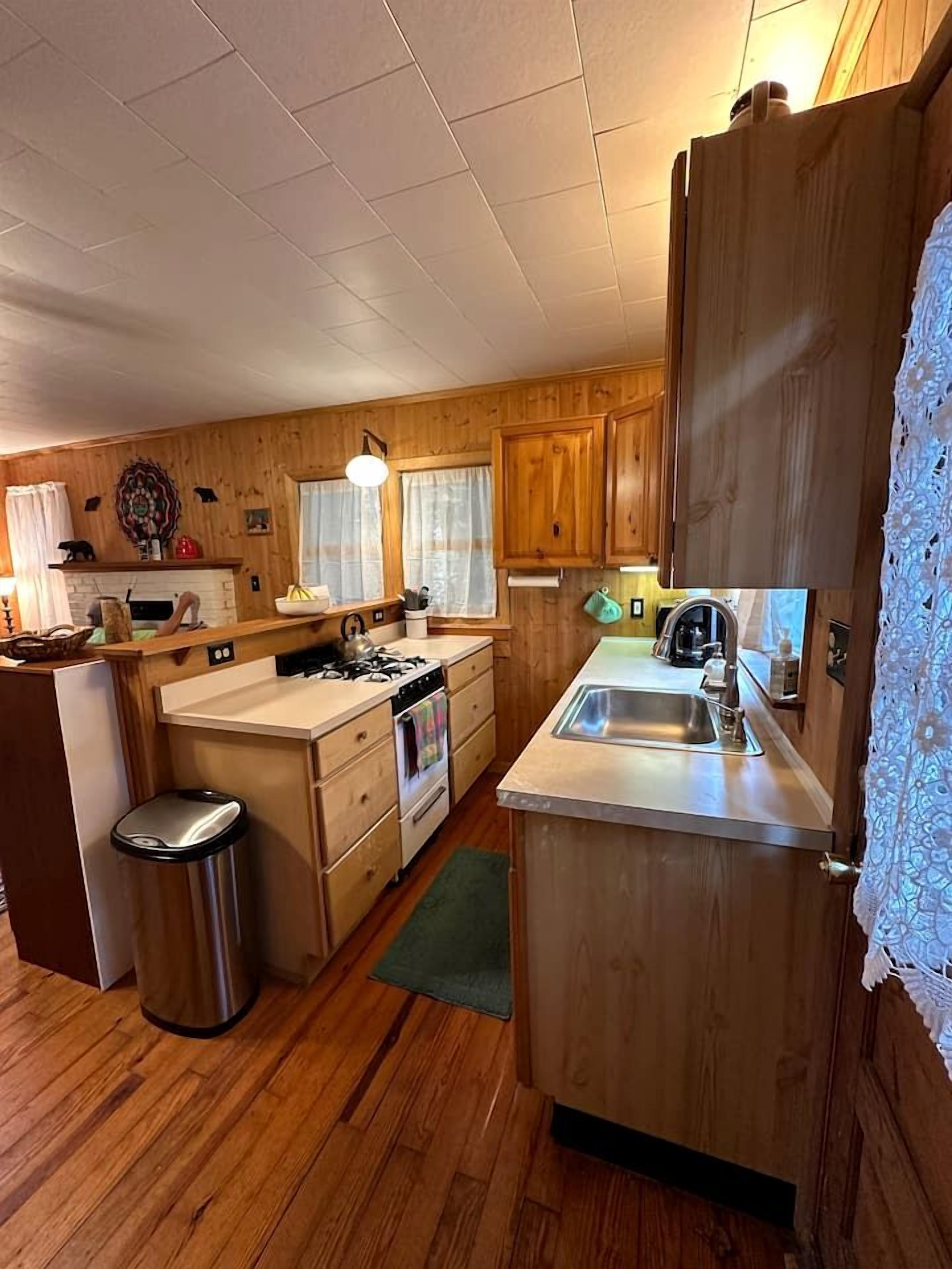 Une cuisine de taille réduite, avec des meubles de rangement en bois, un évier, une cuisinière et une poubelle.