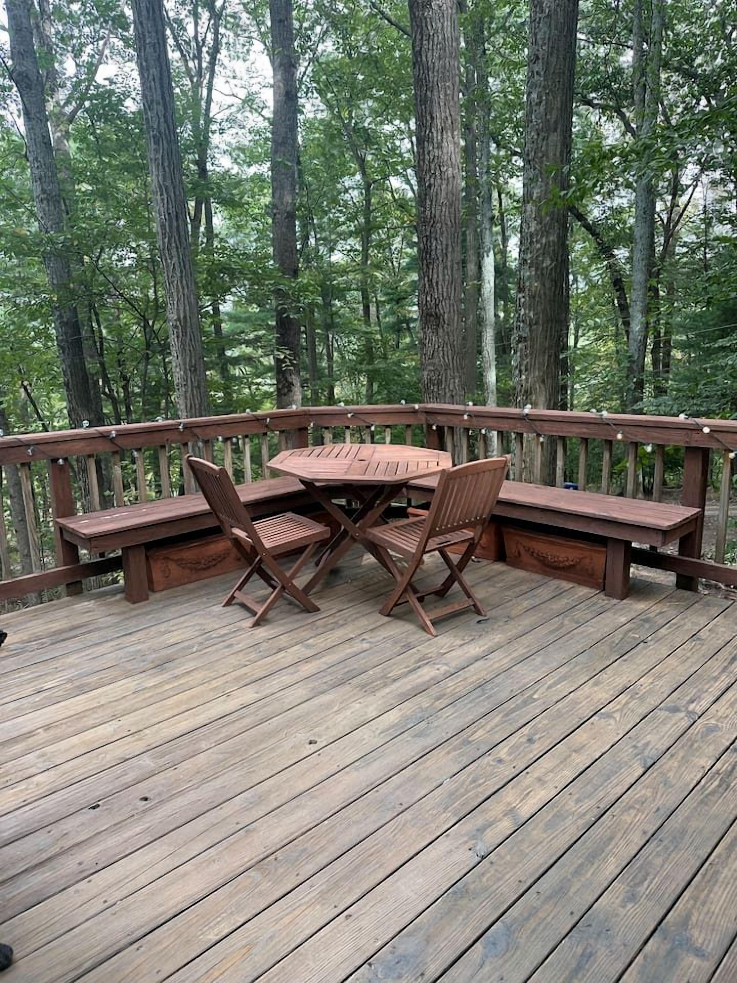 Una terraza de madera con una mesa y sillas, rodeada por barandilla de madera.