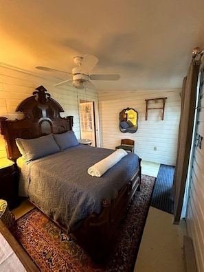 Ein Schlafzimmer mit einem hölzernen Bett, einem Deckenventilator, einem Spiegel und einem kleinen Stuhl.