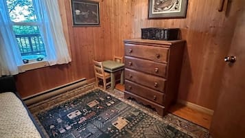 A room with wooden paneled walls, a bed, a dresser, a chair, and a rug.