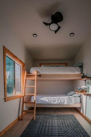 Una camera compatta con un letto a castello, una scala, una scrivania con sedia e una finestra vista alberi.