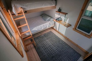 Una stanza compatta con un letto a castello, una scala, un piccolo ripiano con oggetti e una finestra, oltre a un tappeto decorato.