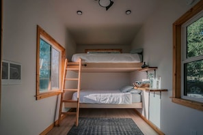 A compact room with bunk beds, a ladder, a window, and a small shelf with items.