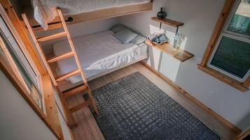 Habitación pequeña con literas, una escalera, un estante con objetos, una ventana y un tapete estampado.
