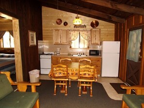 Une cuisine chaleureuse, aménagée dans un style rustique, avec des meubles en bois, une table à manger et des chaises, un réfrigérateur et un four à micro-ondes.