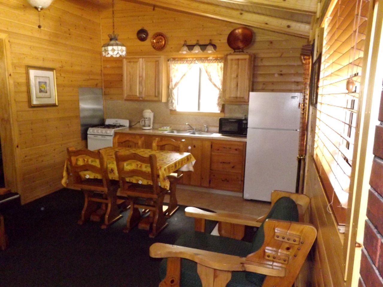 Een houten chalet van binnen met een eettafel, stoelen, een bank en een keukenhoek met een fornuis, koelkast en kasten.